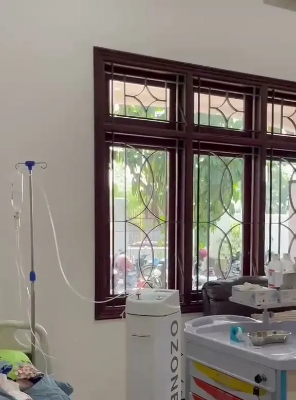 Ruang tindakan Elrhea Clinic: tempat tidur pasien, kursi recliner, tiang infus dan jendela kayu berukir